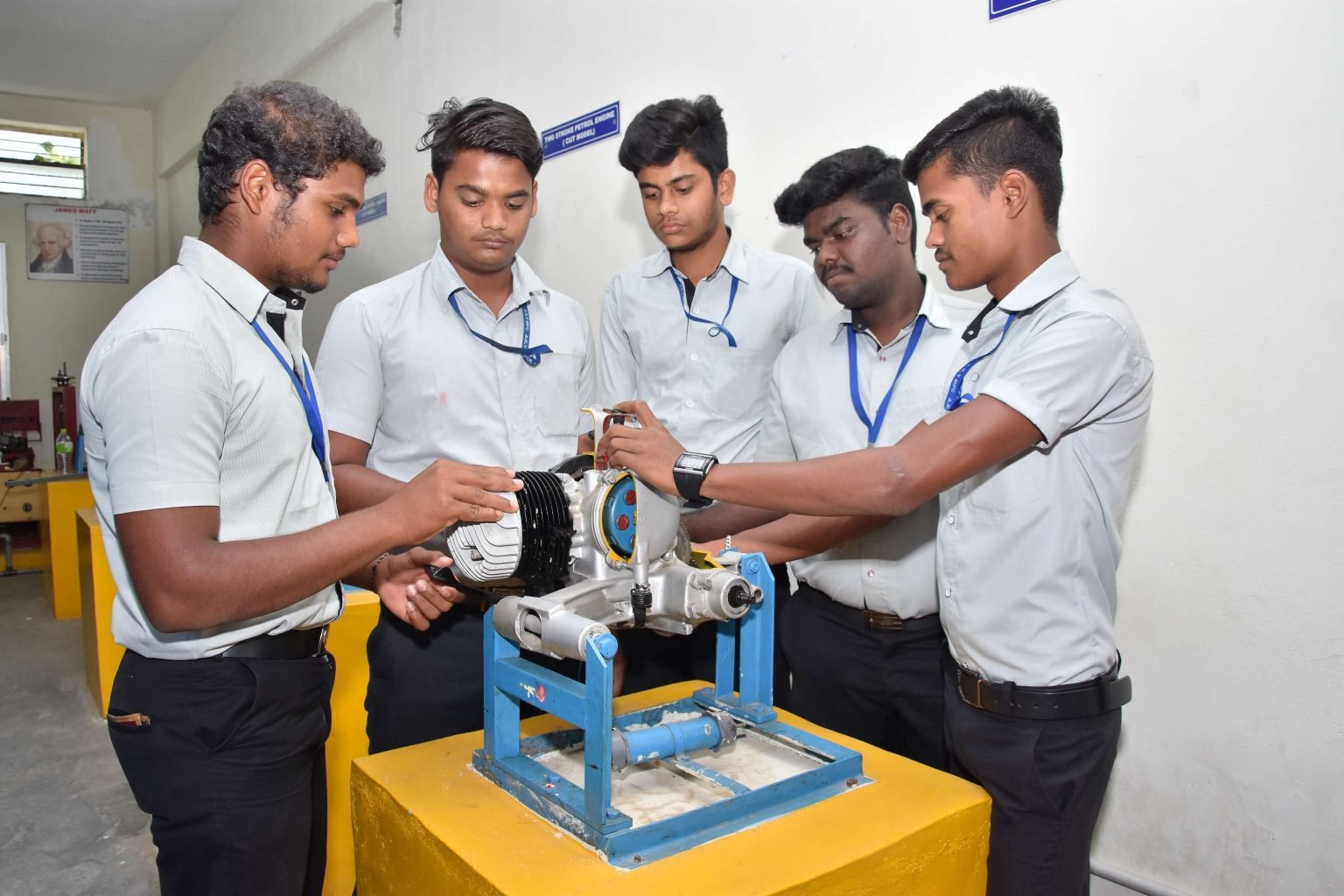 Mechanical students studying a two-stroke engine cut model